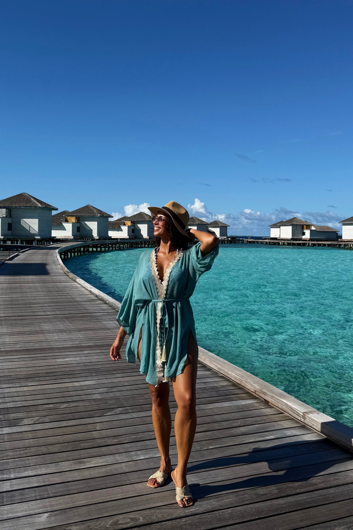 Frau trägt modernen türkisen Kaftan als Sommerkleid am Strand im Urlaub. Leichter Resort Wear Kaftan mit goldenen Details von Sefa Kaftans.