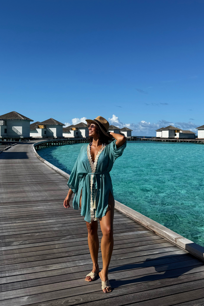 Frau trägt modernen türkisen Kaftan als Sommerkleid am Strand im Urlaub. Leichter Resort Wear Kaftan mit goldenen Details von Sefa Kaftans. 